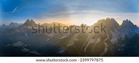Panoramic, arerial view of  sunrise over Tre Cime di Lavaredo and illuminated peaks of the Cime Eotvos mountain massif.  Dolomites, Italy.  Royalty-Free Stock Photo #2399797875