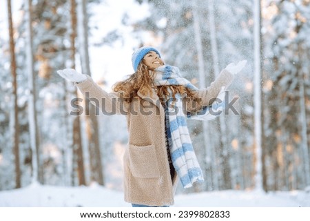 Young woman in warm clothes plays with snow on a sunny winter day. Happy female tourist enjoying a snowy day in the park. Concept of walking, fun. Royalty-Free Stock Photo #2399802833