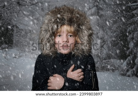 Horizontal photography of cute eight years old boy looking at camera against a background of a winter landscape. He wears a hooded winter eskimo coat. Winter, cold and snow concept
