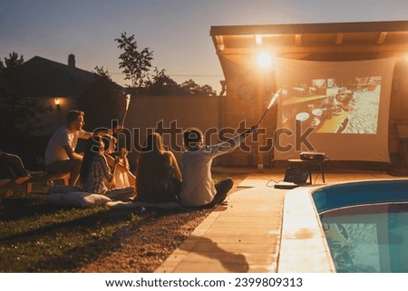 Group of friends having a surprise birthday party in an open air cinema, watching a movie by the swimming pool and waving with sparklers