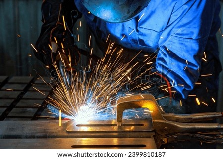 When workers weld using gas argon to steel, sparks are created that result in smoke within factory Royalty-Free Stock Photo #2399810187