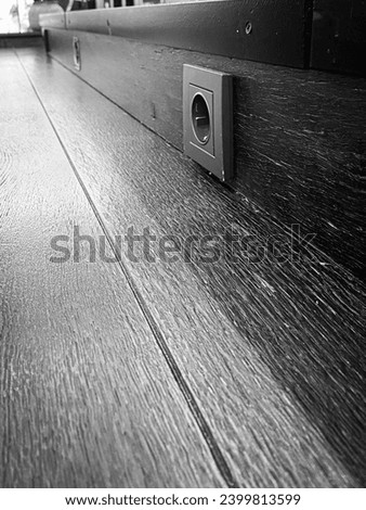 Black and white image of a modern power outlet on a wooden wall near the floor, showcasing minimalist interior design details.