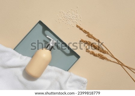 Beige background featured a tray with unbranded pump bottle and white towel displayed on. Rice bran powder not only decongests pores, but also can brighten