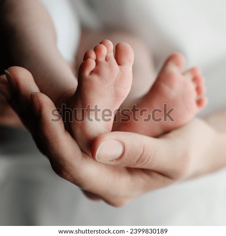 A mother holds the small legs of her newborn baby in her hands, close-up photo.