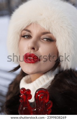 woman with big braids in brown retro fur coat in winter street with snow. Winter cold weather. Girl with candy lollipop in white fur gloves and in high red boots. Smiles. Woman lick lollipop