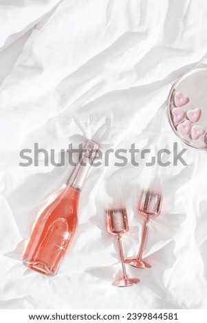 Pink champagne glasses with metal shiny, bottle of rose sparkling wine ,pink candle hearts on bed. Natural daylight, star filter effect. Valentine's Day holiday, love concept, romance evening, above