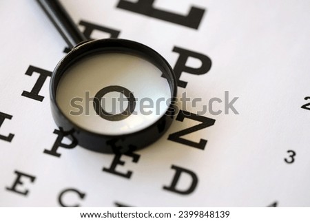 Magnifier glass focuses eye chart letters clearly and lies on eye test chart paper close up