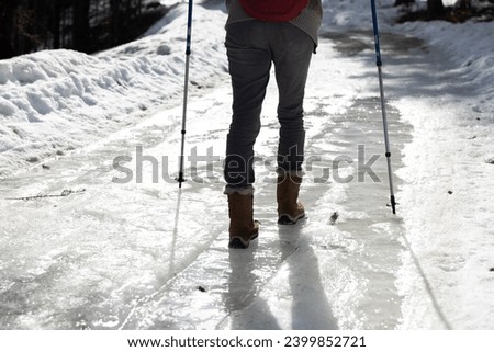 Woman Hiker Walking Carefully over part of Frozen Icy Road in Winter in Snowshoes and with help of Hiking Poles Royalty-Free Stock Photo #2399852721