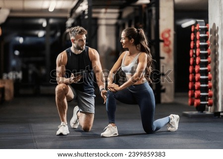 Personal trainer is showing a sportswoman how to do lunges correctly while kneeling in a gym. Royalty-Free Stock Photo #2399859383