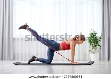 Athletic woman doing exercise with fitness elastic band on mat at home