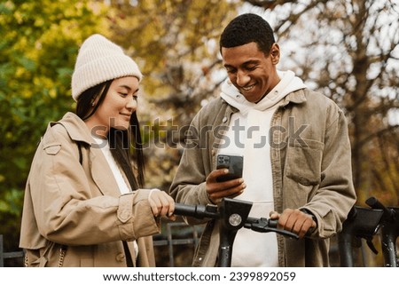 Young multinational couple paying online with smartphone while renting electric scooter in autumn park Royalty-Free Stock Photo #2399892059