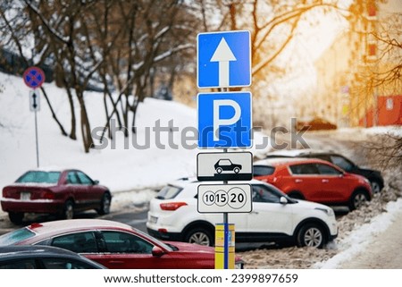 Paid park sign on pole. Row of cars parked on snowy roadside in winter, paid parking sign. Winter parking problems. Crowded snowy parking. Parking management
