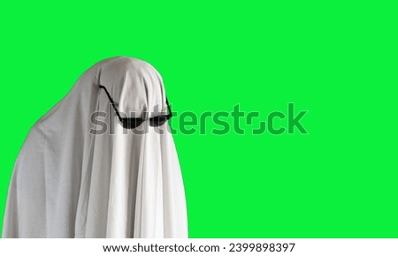 Person in costume of ghost pointing at something on green background with space for text. Halloween celebration    