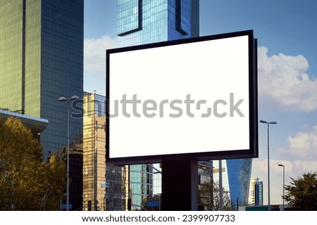 A large information display for advertising on the street in the city, against the backdrop of a skyscraper and a beautiful sky.