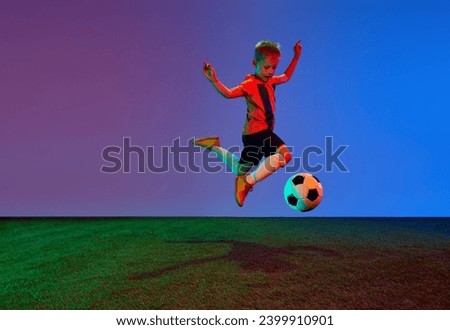 Male beginner soccer player in sports uniform in action, motion with ball over dark blue background in neon. Concept of action, sportive lifestyle, team game, health, energy, vitality and ad