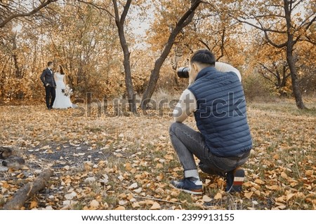 Male wedding photographer taking pictures of the bride and groom in nature in autumn