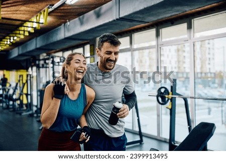 Happy athletic couple laughing while walking through the gym. Copy space. Royalty-Free Stock Photo #2399913495