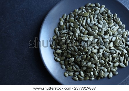 Natural green pumpkin seeds without shell isolated on dark background. Healthy food concept. Overhead view. Copy space. Royalty-Free Stock Photo #2399919889