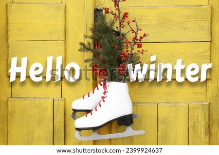 Hello winter. Pair of ice skates with Christmas decor hanging on old yellow door