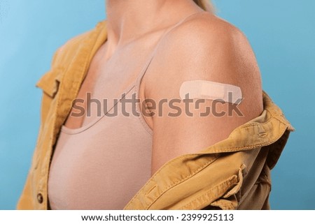 Woman with adhesive bandage on arm after vaccination on light blue background, closeup