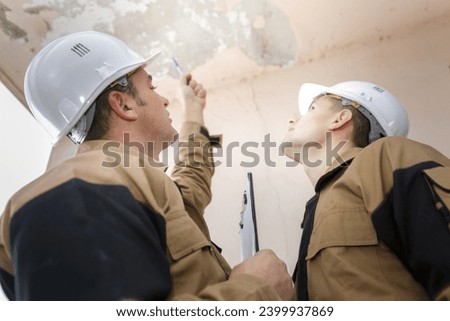 portrait of builders inspecting roof damage Royalty-Free Stock Photo #2399937869