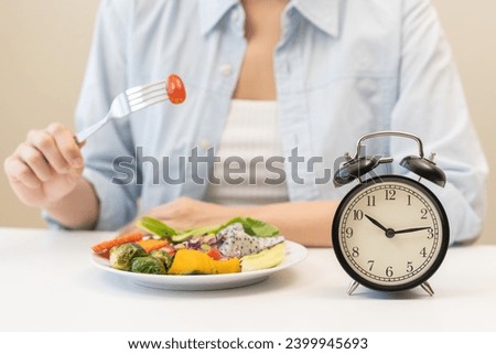 Intermittent fasting with clock, close up young woman, girl diet, waiting time to eat ketogenic low carb, green vegetable salad on plate. Eat food healthy first meal on brunch, lunch on table at home. Royalty-Free Stock Photo #2399945693