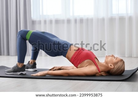 Athletic woman doing exercise with fitness elastic band on mat indoors Royalty-Free Stock Photo #2399953875