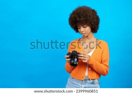 an afro-haired photographer with a camera in her hands reviewing the photos she has taken
