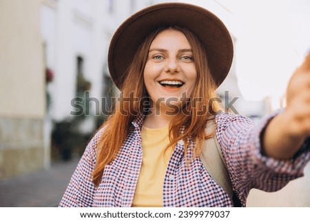 Young beautiful girl in hat say Hi. Photo relaxed charming positive woman hold camera and make selfie summer outside in city center outdoors. Lifestyle tourist travel holiday concept. Point of view.