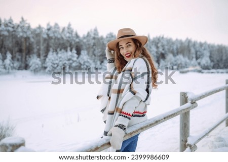 Portrait of a smiling woman in a hat and scarf in a snowy forest enjoying a winter day. Young traveler posing outdoors. Adventure, weekend concept.