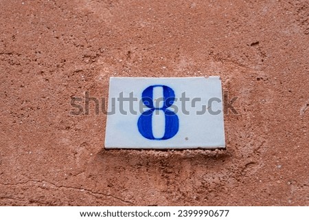 Square white ceramic brick on old wall with the number eight painted in blue color