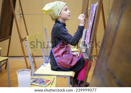 Girl in yellow scarf and apron painting colorful picture in art class
