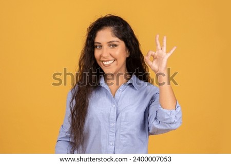 Smiling latin millennial brunette lady in casual show ok sign with hand, recommend sale, isolated on orange studio background. Ad and offer, attention good news, approve gesture Royalty-Free Stock Photo #2400007053