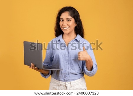Smiling latin millennial brunette woman in casual with laptop show ok sign with hand, success gesture, isolated on orange studio background. Recommendation work, study, chat