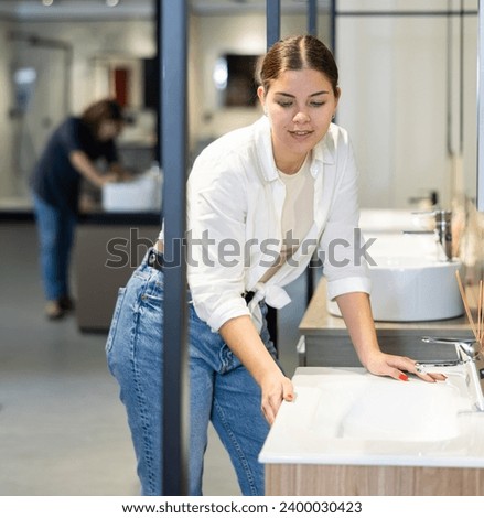 Female buyer compares two plumbing options in window and pays attention to quality and price of goods.woman chooses white ceramic round sink. wide range Royalty-Free Stock Photo #2400030423