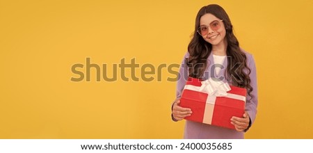 trendy cheerful child in sunglasses and suit hold present box on yellow background. Teenager girl with birthday gift, horizontal poster. Banner header with copy space.