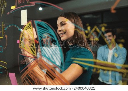 Young beautiful businesswoman writing business plan to investor on glass wall. Skilled female leader presenting marketing strategy by using graph. Smart manager presenting marketing idea. Tracery. Royalty-Free Stock Photo #2400040321