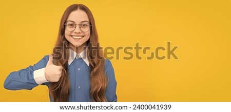Happy nerdy-looking girl child give thumbs up satisfaction hand gesture yellow background, childhood. Child face, horizontal poster, teenager girl isolated portrait, banner with copy space.
