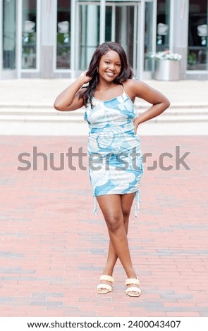 African American female modeling a blue and green flowered dress in an urban setting. Royalty-Free Stock Photo #2400043407