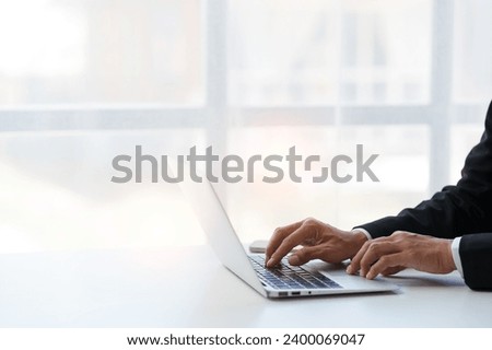 Close up. Asian businessman working with laptop computer at modern office Businessman in black suit working and typing on laptop keyboard Internet online at the desk in the office.
