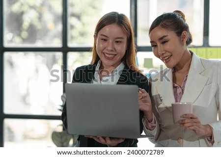 Two Asian businesswomen come up with an idea. Discuss investment projects and strategic planning with information via various documents and files. On a laptop computer at modern office.