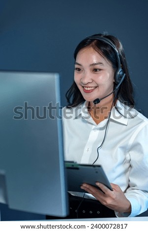 Young Asian call center woman working in a company. Attractive office worker sitting at a desk, wearing a headset and using a PC to talk to support customers, answer questions, explain information.