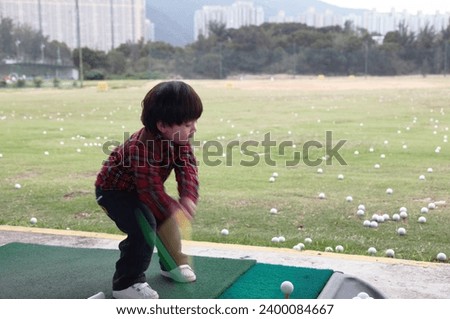 Exterior photo view of a young kid child boy golfer playing golf sport with a speed fast dynamic motion effect when he does his swing to kick the golf ball on a outdoor practice court