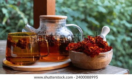 Marigold flower healthy tea in glass mug with tea pot on garden table. Herbal medicine Delicious tisane tea with fresh yellow blossom dandelion flowers tea cup. Green clearing infusion Wildflowers