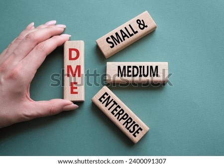 DME - Small and Medium Enterprise symbol. Concept word DME on wooden blocks. Businessman hand. Beautiful grey green background. Business and DME concept. Copy space.