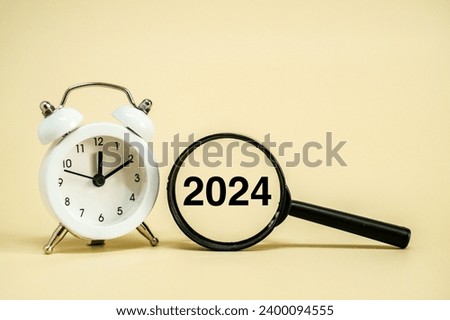 A white alarm clock sitting next to magnifying glass with word "2024"
