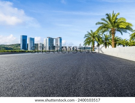 Asphalt road and city buildings with green palm tree under blue sky