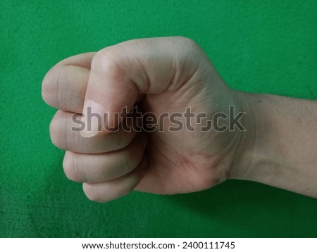 right hand clenched fist against green wall background