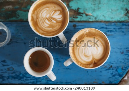 two fresh tasty cappuccino coffee cups with latte art on it and one espresso cup with beautiful tiger crema on the coffee table Royalty-Free Stock Photo #240013189