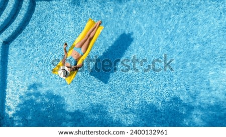 Beautiful woman in hat in swimming pool aerial drone view from above, young girl in bikini relaxes and swims on inflatable mattress and has fun in water on vacation, tropical holiday resort